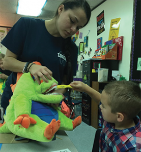 PA student Sabrina Matovich uses Flossisaurus Rex to help a child learn how to brush all surfaces of the teeth.