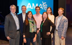 A group of people stand in front of a backdrop that says "AMA"