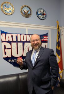a smiling man holds a small red toy car in from of a North Carolina National Guard banner