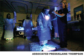 During a training demonstration at Madigan Army Medical Center on Joint Base Lewis McChord, near Tacoma, Wash., a medical worker wearing personal protective equipment is illuminated with a black light to look for traces of ultraviolet-responsive liquid that represents fluids, which could transmit the Ebola virus.